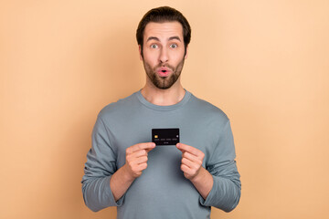 Photo of young guy impressed hold bank card salary profit face reaction isolated over beige color...