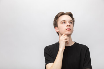 Thoughtful young man with hand on chin studio shot on gray background