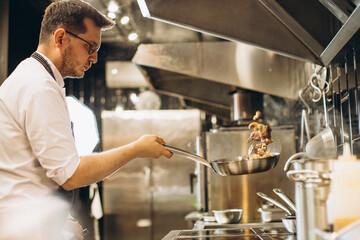 Man chef frying meat in a pan in fire