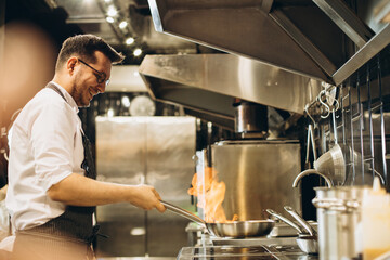Man chef frying meat in a pan in fire