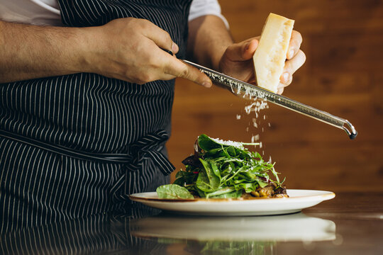 Male chef at kitchen preparing salad rubbing cheese on top