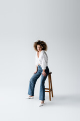 Stylish model in blouse posing near chair on white background.