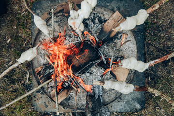 A camp fire. Sticks with dough are being held above it in order to make bread.