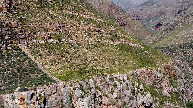 Aerial drone shot ascending up revealing the arid rocky mountainous landscape which surrounds the Meiringspoort pass, a scenic route which travels through the Swartberg Mountain range, South Africa