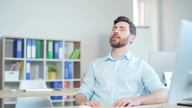 Male worker relaxes with eyes closed and takes a deep breath. enjoys the cold and fresh air in the room. Sitting on workplace in the office indoors at work. Man employee entrepreneur a computer desk
