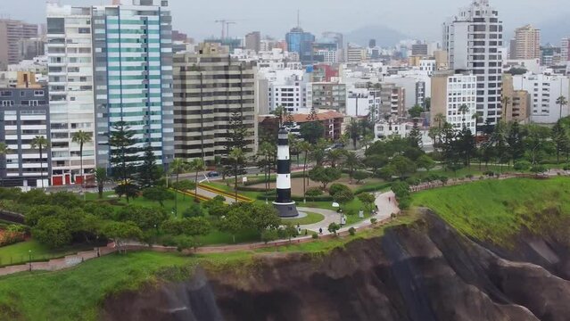 Drone video of a lighthouse in Miraflores. In Lima Peru. Far away parallax shot with many buildings in the background visible and parks on the green hills.