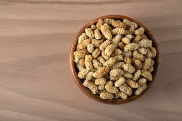 Bowl full of dried mulberry on a wooden background	