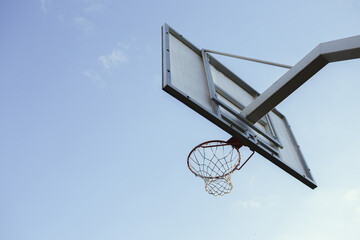 Low angle of basketball backboard with hoop rim and net on urban court on background of blue sky in sunset 