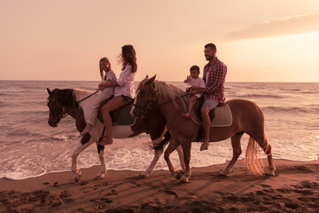 The family spends time with their children while riding horses together on a sandy beach. Selective focus 