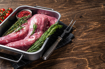 Fresh raw pork tenderloin meat, uncooked fillet in kitchen tray with herbs. Wooden background. Top...
