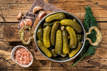 Pickled gherkins cucumbers in bowl with herbs. Wooden background. Top view