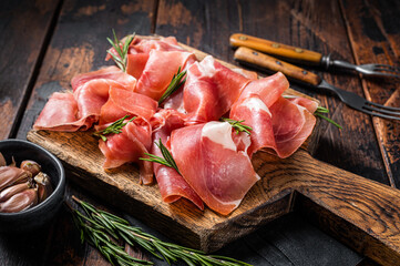Slices of jamon serrano ham or prosciutto crudo parma on wooden board with rosemary. Wooden background. Top view - obrazy, fototapety, plakaty