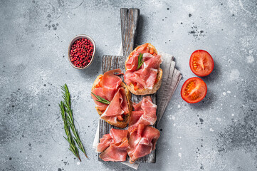 Spanish Tapas - Toast with tomatoes and cured Slices of jamon iberico ham on wooden board. Gray...