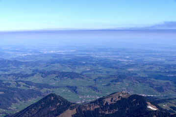 Aerial view with Mountains and midland in the background seen from Säntis peak at Alpstein Mountains on a sunny spring day. Photo taken April 19th, 2022, Säntis, Switzerland.