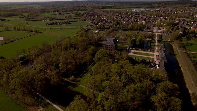 Sideways aerial reveal of Dutch painterly picturesque moated castle Amerongen surrounded by gardens and park with the village town and countryside meadows in the background