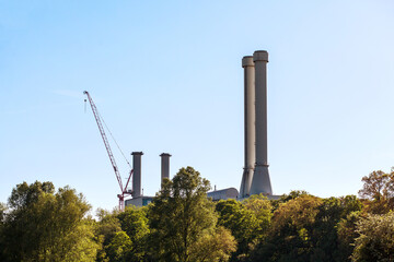 Fototapeta na wymiar Plant Pipes Chimneys of Waste Processing Plant. Industrial enterprise chimneys. Giant smoke stack in industrial area behind trees.
