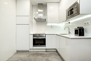 Kitchen with white furniture and stainless steel appliances, white stone countertop with small appliances on it in an apartment with sloping ceilings.
