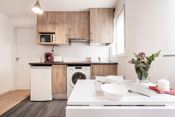 Kitchen with white furniture and stainless steel appliances, white stone countertop with small appliances on it in an apartment with sloping ceilings.