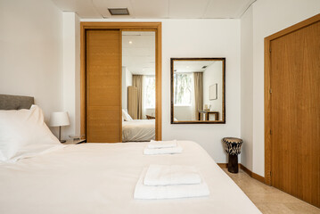 Fototapeta na wymiar Bedroom with Venetian wooden sliding door wardrobes, mirrors and white towels on the bed