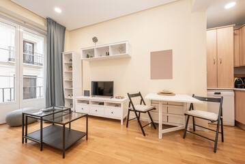 Fototapeta premium Living room with white wooden furniture, matching folding dining table, open kitchen in a corner and balcony to the street