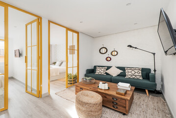 Living room with blue three-seater sofa, vintage wooden side table, metal and glass doors painted yellow and rattan rug