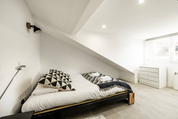 Bedroom with white sloping ceilings, bed with futon and white chest of drawers with white aluminum...