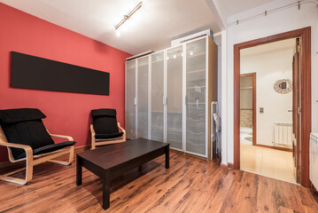 living room with brown wood flooring, black wood folding side table, door to hallway and gray metal and glass door cabinet