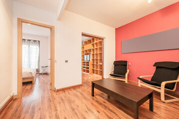 living room with brown wooden floor, black wooden folding side table, beech wood armchairs with black upholstery and red painted wall