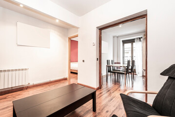 living room with brown wooden floor, black wooden folding side table, beech wood armchairs with black upholstery and access to office with chromed metal boardroom table and glass with black armchairs