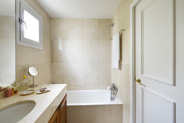 Toilet with shower cabin, cream-colored marble tiles and countertop with a white sink on wooden cabinet with grids
