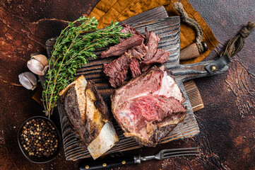 Braised veal beef short ribs on wooden cutting board with thyme. Dark background. Top view