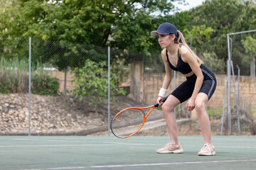 Young woman focused on the tennis match in which she is participating as a player. With bent legs on a black outfit