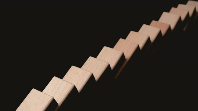 Row of wooden domino falling down against black background. Domino effect.