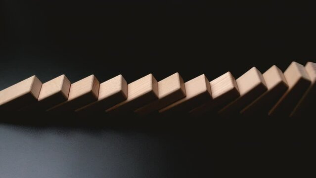 Row of wooden domino falling down against black background. Domino effect.