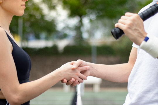 Close up view of man and woman tennis players hand shaking in the middle of a tennis court with net below