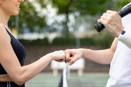 Close up view of two unrecognizable tennis players knuckle bumping to each other on a tennis court