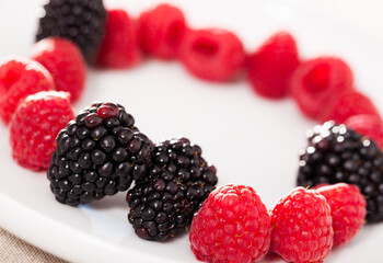 raspberries and blackberries laid out on a white plate in circle