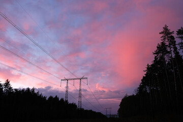 Silhouette of high voltage electricity tower with wires and forest trees against dramatic twilight...