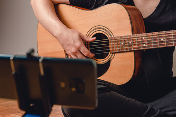 Fototapeta premium unrecognizable Latin man sitting on the floor playing guitar in front of a phone on a tripod