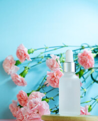 Blank transparent beauty serum dropper on  blue background with blooming pink carnation flowers. Beauty care concept advertisment poster.