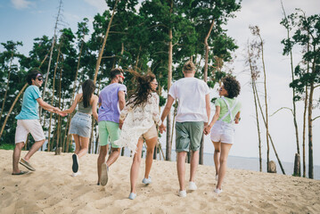 Full size rear behind photo of excited positive people running walking sand beach hold hands warm...