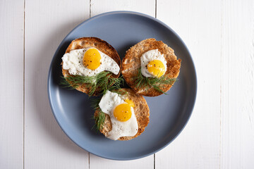 Fried quail eggs baked in round rolls on a blue plate and white wooden background
