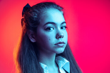 Close-up portrait of young girl, student posing, looking attentively at camera isolated over pink background