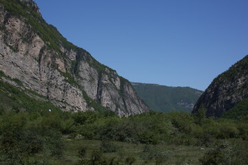 Naklejka premium Caucasian mountains in sunny weather, green dense forests on the mountains and snowy peaks of the old high mountains of Georgia