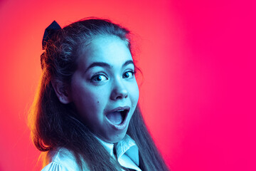 Close-up portrait of young girl, student posing, showing emotion of excitement isolated over pink background in neon light