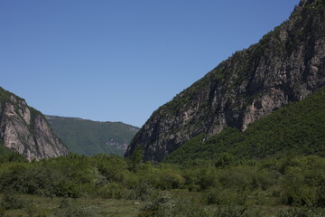 Caucasian mountains in sunny weather, green dense forests on the mountains and snowy peaks of the old high mountains of Georgia