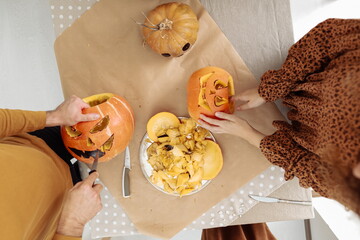 Young couple man and woman on kitchen at home making jack-o'-lantern preparing for halloween, cutting pumpkin. Cutting out faces from a fresh pumpkin. Preparing for the Halloween party celebration.