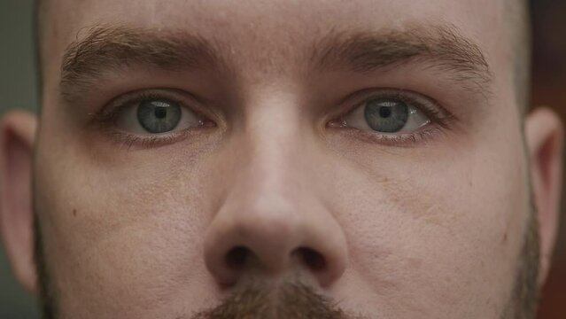 Close-up of a young adult caucasian man opening his blue eyes in slow motion