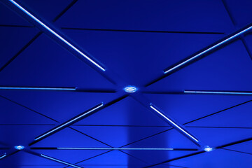 An example of the exterior application of LED strip lighting flush mounted in a blue metal ceiling of a covered building entrance, nobody