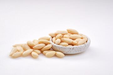 Pile of peeled or blanched almonds. White bowl of peeled whole almonds on white background. Shallow depth of field